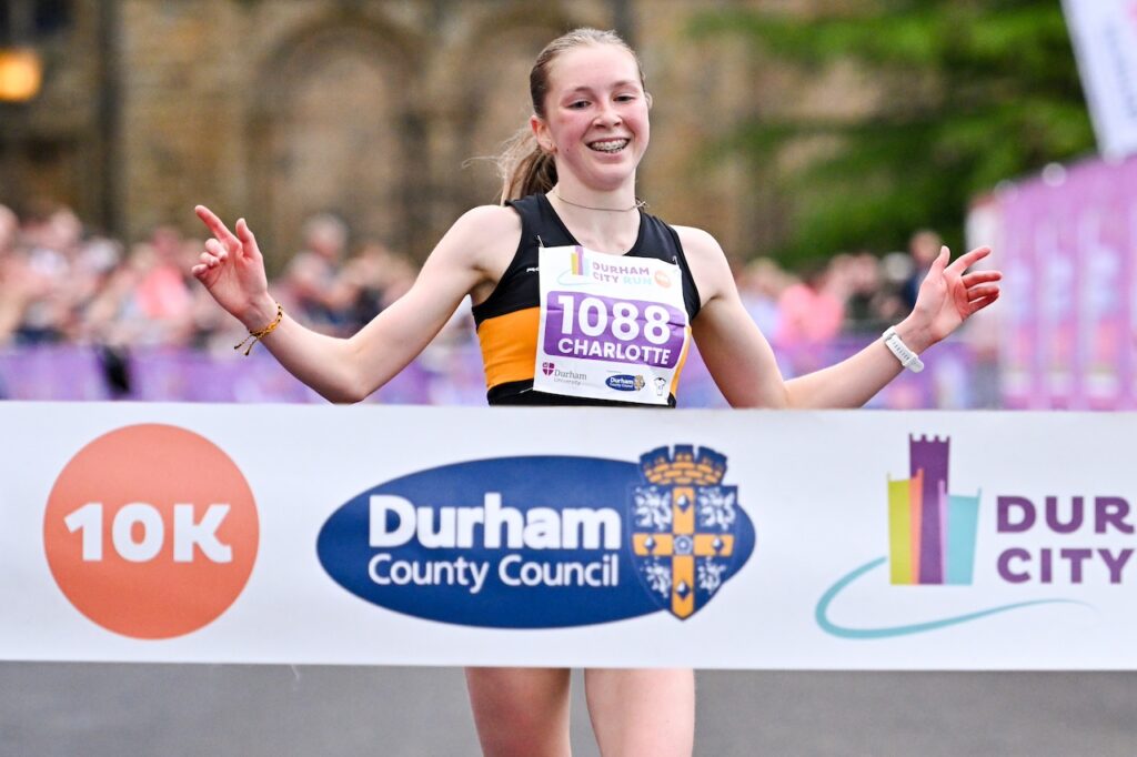 Runner with arms in the air crossing the finish line at Durham City Runs.