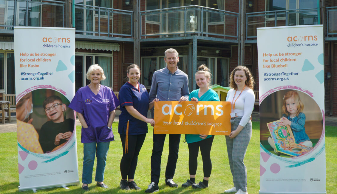 Five people standing next to pop up posters for Acorns Children's Hospice.